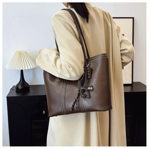 Detail of dark brown leather tote bag with white stitching and cat charm for daily use