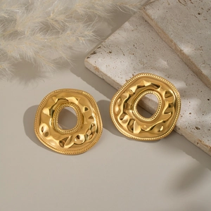 Irregular golden donut earrings with hammer texture shown on decorative stone base