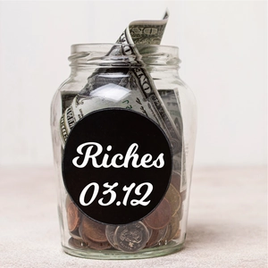 Clear glass money jar filled with coins and bills with a black Riches label sticker