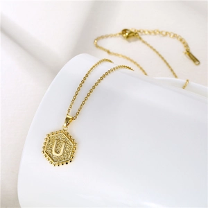 Macro detail of hexagonal gold pendant with letter U engraving on white ceramic stand