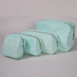 Set of four mint green nylon cosmetic bags with gold zippers on light grey background