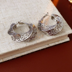 Macro detail of silver geometric twisted hoop earrings with cutout Greek key patterns