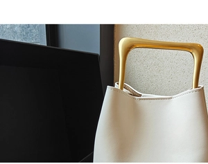 Detailed close-up of cream leather texture and unique gold metal handle on bucket bag