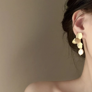 Detailed view of golden flower petal earrings with a baroque pearl on a female model
