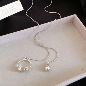 Detail of silver snake chain necklace with mini headphone and teardrop pendants on tray