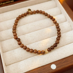 Detailed close-up of dark brown wooden bead bracelet with gold charm in a jewelry box