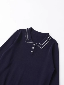 Detailed view of dark blue knit polo shirt with white wavy collar and button closure