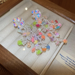 Macro detail of handmade beaded tassel earrings with colorful smile charms in a wooden box