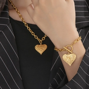 Detail of gold heart pendant necklace and bracelet set with embossed patterns and OT buckle