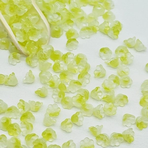 Macro shot of pale yellow lily of the valley glass flower beads on a wooden scoop