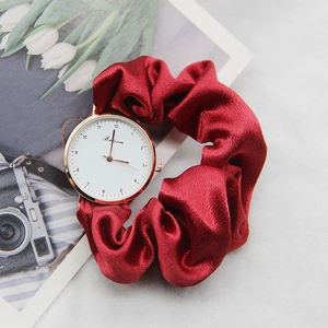 Close-up of elegant gold watch with a red ribbon fabric scrunchie strap on a magazine
