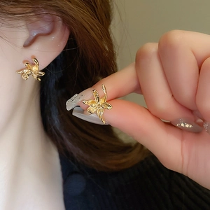 Detailed close-up of golden metal flower earrings on ear with irregular pleat design