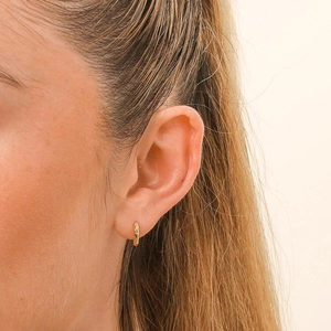Close-up of a model wearing a textured golden s925 silver hoop earring on a clean background