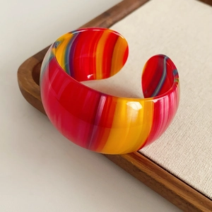 Detailed view of rainbow striped acetate open bangle on a warm wooden display tray