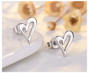 Macro detail of polished silver heart earrings on elegant white ceramic base