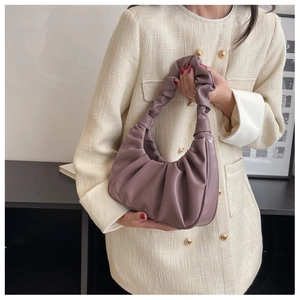 Detail showing soft purple pleated cloud handbag held by model in beige jacket