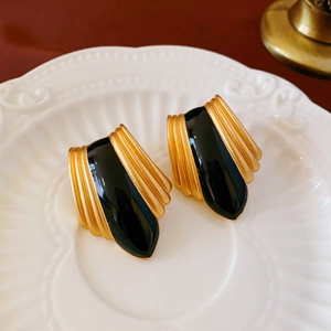Close-up of vintage gold and black enamel teardrop earrings on a white ceramic plate