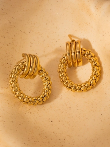Close-up of golden geometric earrings with textured circular patterns and luxury finish
