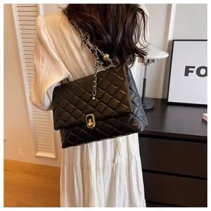 Quilted black shoulder bag with gold chain strap shown on model in stylish interior