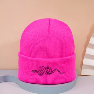 Close-up of bright pink knitted beanie with black snake embroidery on a wide cuff