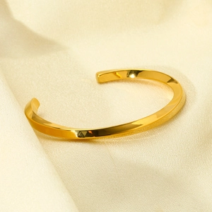 Detail shot of a polished 18k gold-plated twisted cuff bracelet on silk fabric
