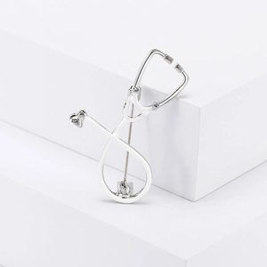 Macro detail of a silver stethoscope brooch pinned to a clean minimalist white background
