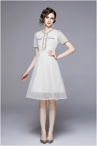 Detail of white lace dress with black and gold woven trim and pearl button accents