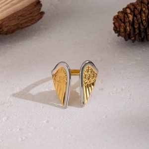 Detailed view of two-tone angel wing ring on natural wood with pine cone decor