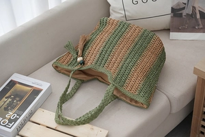 Detail of green and brown striped straw tote bag with fringe charm on a sofa