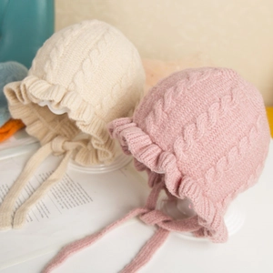 Detailed knit texture and ruffle edge of beige and pink baby beanies with chin straps
