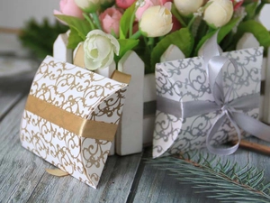 Detail of elegant pillow candy boxes with gold and silver baroque patterns and silk ribbons