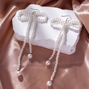 Detailed view of bow-shaped pearl tassel earrings on a rose gold silk background