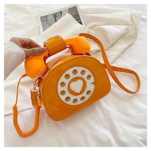 Detail of creative vintage telephone-shaped crossbody bag in glossy orange patent leather