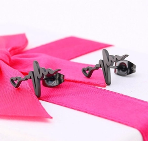 Macro detail of black heart pulse earrings placed on a pink ribbon gift bow