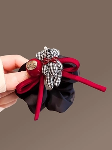 Detail of checkered bear and red velvet bow on a black silk scrunchie hair accessory