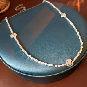 Macro detail of silver smiley face pendants on a square-beaded choker necklace