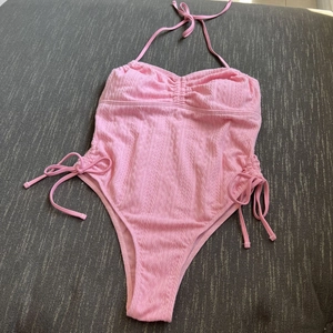 Detailansicht eines rosa Badeanzugs mit strukturierter Oberfläche und seitlichen Kordelzügen