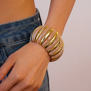 Detail of pink resin and gold metal beads on an elastic bracelet worn by a model