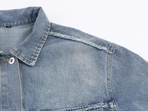 Detailed macro of mid-blue denim jacket showing frayed edges and metallic buttons