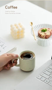 Close-up of a hand holding a speckled Morandi ceramic mug in a cozy coffee setting