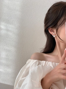 Close-up of elegant double butterfly pearl earrings worn by a model on a grey background