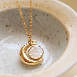Elegant gold celestial necklace featuring moon and sun shell pendant on a porcelain bowl