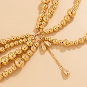 Detail of multi-layer golden beaded body chain featuring teardrop pendants and tassels