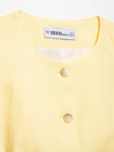 Close-up of yellow linen tank top neckline featuring wood-textured buttons and size label