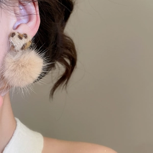 Close-up of leopard heart stud with beige faux fur pom-pom earring worn by a model
