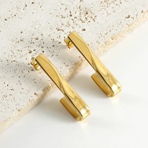 Detail of twisted gold hook earrings displayed on natural beige stone texture
