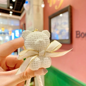 Macro detail of white resin bear keychain featuring knit texture and gold-edged satin bow