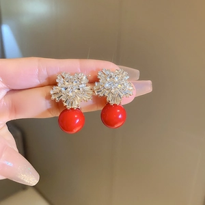 Detailed close-up of zircon flower earrings with red pearls held by hand in soft light