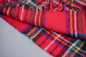 Detail of red plaid acrylic cape showing fabric texture and soft tassel fringe finish