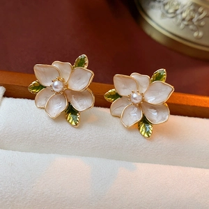Macro shot of white enamel flower earring with pearl center and green leaf detail